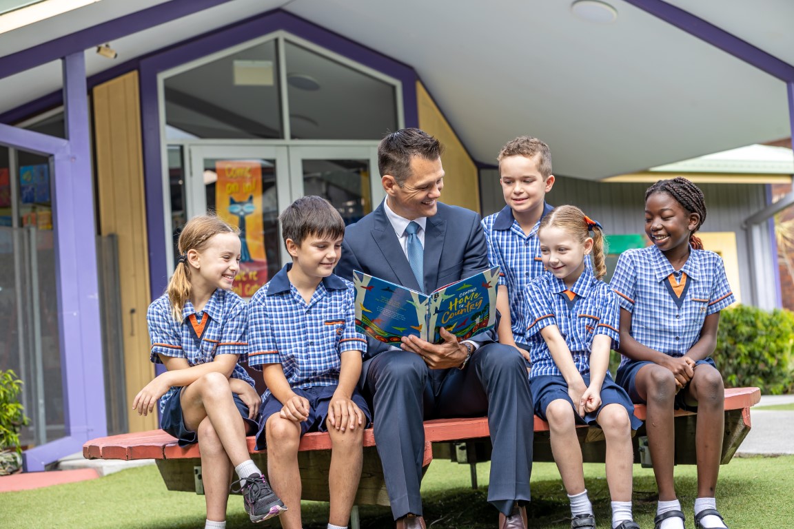 Adult reading a book to a group of students outside.