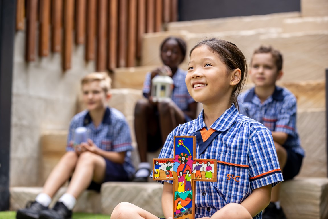 Student holding a colourful cross with other students seated behind her